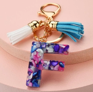 Detail of resin letter F keychain with colorful stones, gold chain and double tassels
