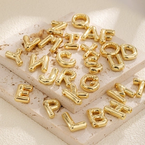 Gold-plated bubble letter pendants set A-Z for DIY necklaces on a stone tray