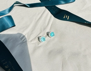 Macro shot of 8mm Paraiba blue gemstones set in 925 silver halo earrings on silk fabric