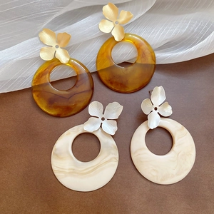Detailed close-up of acrylic resin hoop earrings with textured metal flower studs in gold and silver