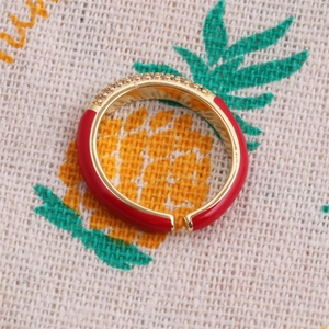 Macro detail of red enamel gold ring with zircon pavé on pineapple print fabric