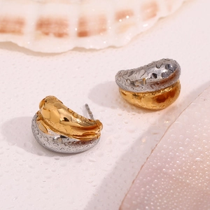 Detail of two-tone gold and silver earrings with water droplets on shell background