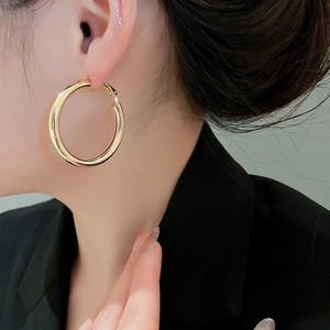 Close-up of chunky polished gold round hoop earrings worn by a model in black blazer