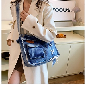 Detail of blue washed denim crossbody bag with raw edges and white ribbon bow decoration