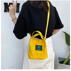 Detail of yellow canvas bucket bag with adjustable strap and green logo patch