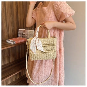 Detail of straw handbag with silk scarf wrapped handle and shoulder strap held by model