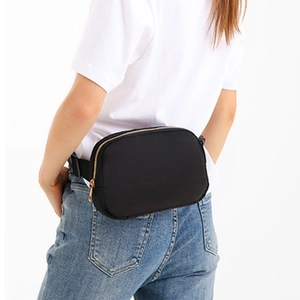 Black waterproof nylon belt bag with gold zippers worn as a crossbody athletic pack