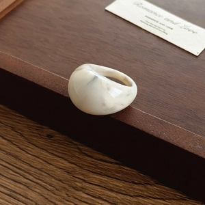 Détail d'une bague en résine épaisse avec texture marbrée grise sur boîte en bois
