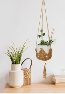 Detail of hand-woven macrame plant hanger with brown twine tassels and white ceramic pot