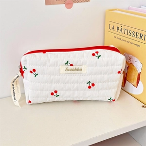Close-up of white quilted cherry print pouch with red zipper and embroidery detail