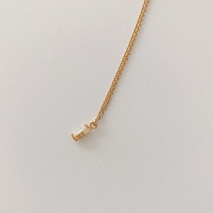 Detail of a minimalist gold necklace with a baguette-cut zircon pendant on textured paper