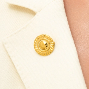 Detailed view of a vintage gold sunburst brooch on a white woolen coat lapel