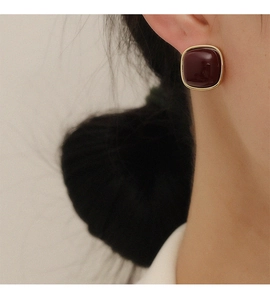 Close-up of square burgundy stud earring with gold metal frame worn on ear