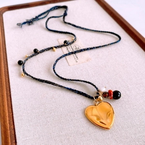 Gros plan du pendentif cœur doré sur collier en corde tressée bleue avec perles