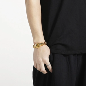 Close-up of a chunky gold Cuban chain bracelet with plug-in clasp on a male model's wrist