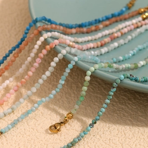 Detail view of colorful faceted stone anklets with gold lobster clasp on ceramic plate