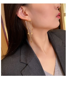 Close-up of elegant gold star tassel earrings with long metallic chains on a model