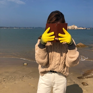 Detail of yellow knit touchscreen gloves with grey cuffs worn in a beach setting