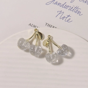 Detail of glittery resin cherry charms with gold metal stems on a white textured plate