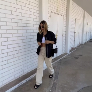 Women's casual black bomber jacket paired with beige cargo pants on a street background