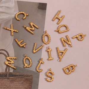 Macro detail of 18K gold plated twisted metal letter pendants in a vintage aesthetic