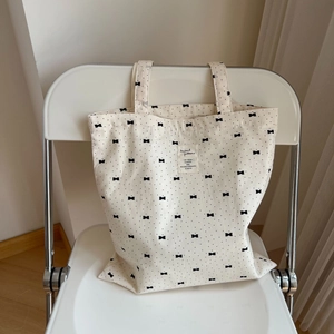 Minimalist beige floral cotton tote bag with black bow print on a stylish white chair