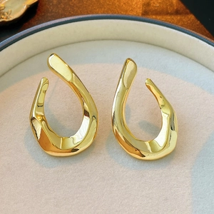 Close-up of golden irregular twisted teardrop earrings with high-gloss metallic finish