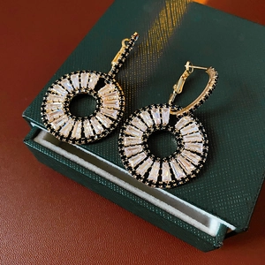 Detail of gold zircon geometric earrings on a luxury green velvet jewelry box