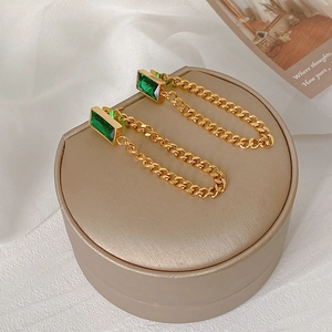Boucles d'oreilles chaînes dorées avec pierres vert émeraude sur boîte à bijoux