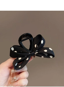 Détail d'une pince à cheveux avec nœud à pois noirs et blancs tenue à la main