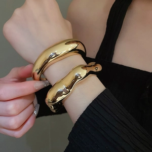 Detail of chunky gold bracelets with smooth and wavy polished metal textures on wrist