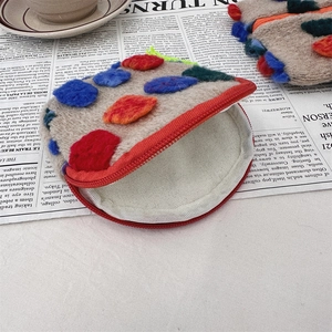 Detail of a vintage round pouch with colorful felt dots and a red zipper on newspaper