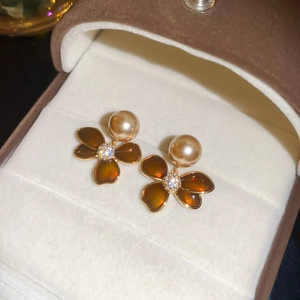 Macro detail of amber enamel clover earrings with champagne pearls in a jewelry box