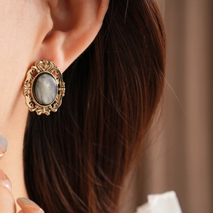 Close-up of vintage golden earrings with dark iridescent resin inlay on female model