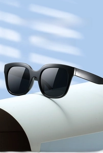 Detail of square black oversized sunglasses on a minimalist stand with soft lighting