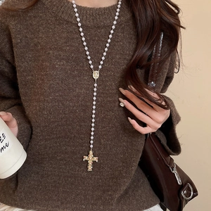 Close-up of a pearl cross necklace with Madonna pendant on a dark sweater for women