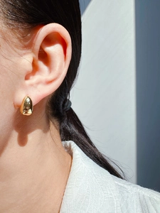 Macro shot of minimalist gold teardrop earring worn by a model in soft lighting