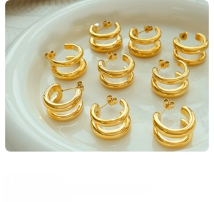 Close-up of golden double-layer C-shaped earrings on a white ceramic display tray