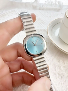 Detail of silver women's watch with light blue dial held against a white tea cup