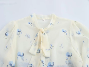 Dettaglio della camicetta in chiffon floreale con fiocco al collo e maniche a sbuffo