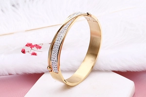 Macro shot of gold stainless steel wide bangle featuring cross design and paved diamonds