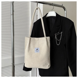 Close-up of cream textured tote bag with blue leaf label hanging on a metal rack