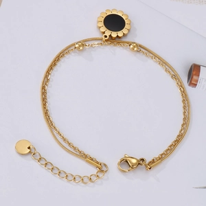 Detail of double-layered gold snake chain bracelet with black sunflower pendant
