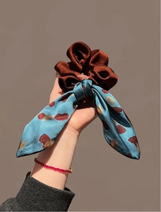Detail of elegant two-tone velvet scrunchie with printed satin bow held in hand