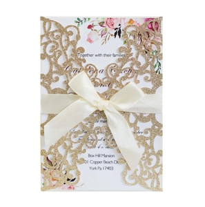 Detail of laser-cut glitter navy invitation with floral card and beige ribbon bow