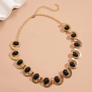 Macro detail of gold U-link necklace featuring oval black resin stones on warm background