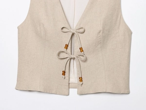Detail of beige linen vest with tie-front closure and brown wooden bead decorations