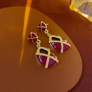 Détail de boucles d'oreilles vintage en or et émail bordeaux sur un fond texturé sombre