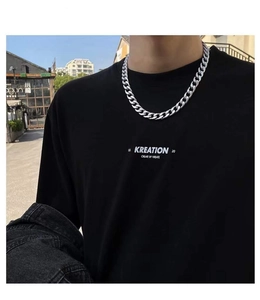 Street style view of a thick silver Cuban link chain necklace worn on a black t-shirt