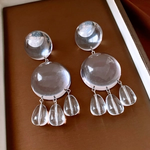 Detailed view of clear resin drop earrings with geometric spheres on a leather tray